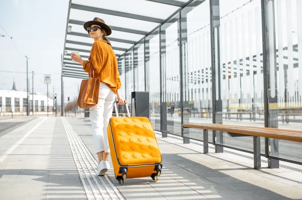 オレンジのスーツケースをひいている女性